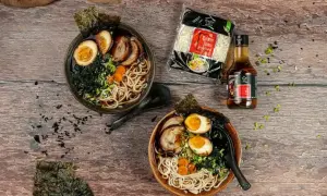 Dwie miski domowego ramenu z jajkiem, mięsem i nori, obok makaron i sos.
