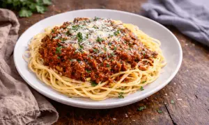 Talerz spaghetti z sosem bolońskim, posypany parmezanem i natką pietruszki.