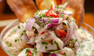 Ceviche z ryby, cebuli, papryczki chili i kolendry w szklanej misce, z chipsami bananowymi w tle.