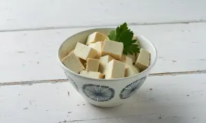 Miseczka z pokrojonym w kostkę tofu i listkiem pietruszki na białym, drewnianym tle.