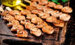 Grillowane krewetki na drewnianej desce, skropione oliwą.
