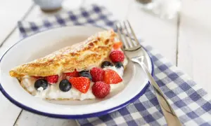 Puszysty omlet z serkiem i owocami leśnymi na talerzu.