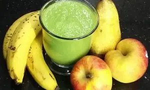Zielony koktajl w szklance otoczony bananami, jabłkami i gruszką.