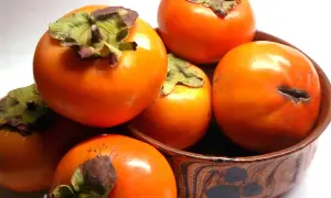 Kilka pomarańczowych owoców persymony (kaki) w drewnianej misce.