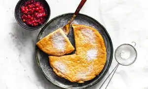 Puszysty omlet posypany cukrem pudrem, podany z żurawiną i łyżką.