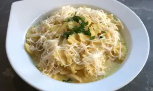 Szybki obiad z twarogiem: makaron farfalle w kremowym sosie, posypany startym serem i natką pietruszki.