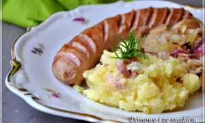 Biała kiełbasa z ziemniakami i kapustą kiszoną, udekorowana koperkiem.