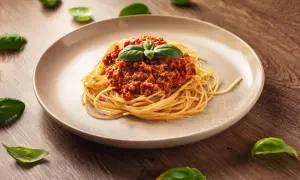 Talerz spaghetti z sosem bolońskim i listkami bazylii na drewnianym tle.