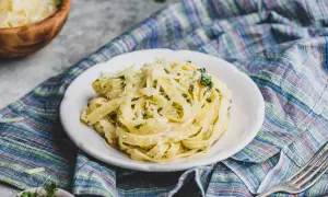 Talerz makaronu tagliatelle z kremowym sosem, posypany startym parmezanem i ziołami, na kolorowym obrusie.