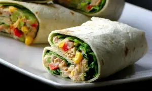 Tortilla z tuńczykiem, kukurydzą, papryką i sałatą na białym talerzu.