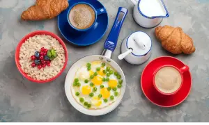 Jajecznica z groszkiem, owsianka z owocami, dwa croissanty i kawa na szarym tle.