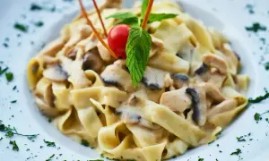 Tagliatelle z kurczakiem i grzybami w sosie śmietanowym, udekorowane pomidorkiem i miętą.