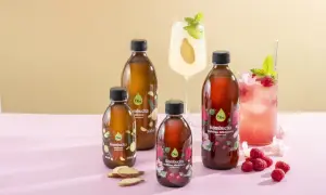 Butelki z kombuchą, drinki, maliny i imbir na różowym tle.