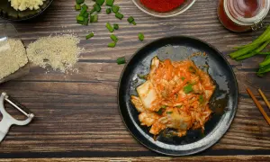 Talerz z kimchi, obok składniki: sezam, czosnek, papryka, szczypiorek, obieraczka i pałeczki.