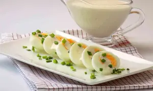 Jajka na twardo polane sosem i posypane szczypiorkiem, obok sosjerka z sosem.