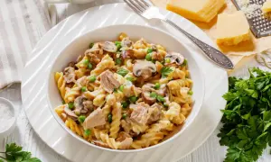 Makaron fusilli z tuńczykiem, groszkiem i pieczarkami w kremowym sosie, udekorowany natką pietruszki.