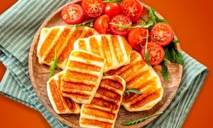 Grillowany ser halloumi z pomidorkami koktajlowymi na drewnianej desce.