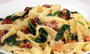 Makaron tagliatelle z kremowym sosem, szpinakiem i kawałkami boczku.