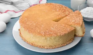 Puszysty biszkopt na talerzu, obok jajka, mąka, mleko i trzepaczka.