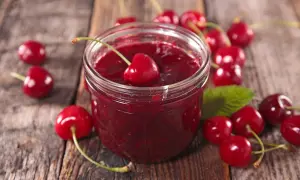 Słoik z wiśniową konfiturą i świeżymi wiśniami na drewnianym tle.
