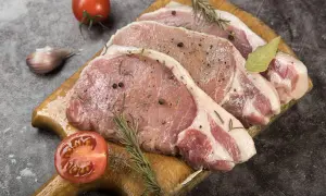 Surowe plastry schabu z przyprawami, rozmarynem, czosnkiem i pomidorem na desce.