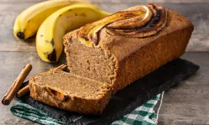 Wilgotny chlebek bananowy z plasterkami banana na wierzchu, obok banany i laski cynamonu.