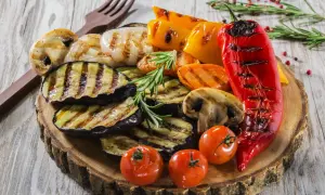 Grillowane warzywa: bakłażan, papryka, pieczarki, pomidorki i marchewka na drewnianej desce.
