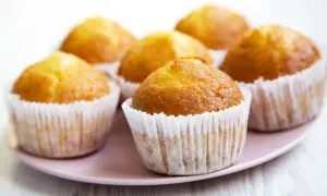 Kilka złotych muffinek w papierowych foremkach na różowym talerzu.