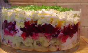 Warstwowa sałatka w szklanej misie: buraki, jajka, ziemniaki, majonez, posypana zieloną pietruszką.