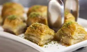 Słodka baklava z pistacjami na białej tacy, z widocznymi szczypcami do serwowania.