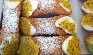 Sycylijskie cannoli z kremem i pistacjami, posypane cukrem pudrem.