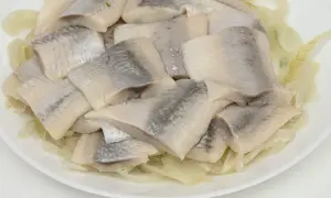 Kawałki śledzia ułożone na talerzu z pokrojoną cebulą.