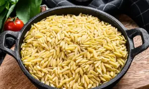 Makaron orzo w czarnej patelni, obok pomidorów i ziół.