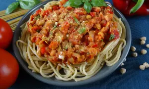 Talerz spaghetti z sosem z ciecierzycy, pomidorami, papryką i bazylią.