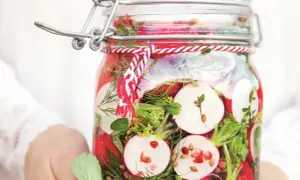 Słoik z kiszonymi rzodkiewkami, ziołami i przyprawami, ozdobiony sznurkiem.