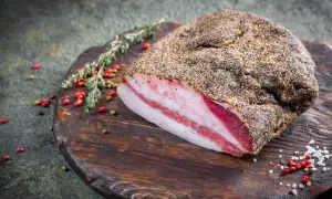 Kawałek guanciale z widocznymi warstwami tłuszczu i mięsa, przyprawiony pieprzem, na drewnianej desce.