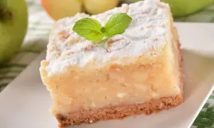 Kawałek ciasta z jabłkami, posypany cukrem pudrem i udekorowany listkiem mięty.