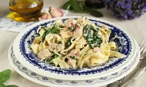 Makaron tagliatelle z tuńczykiem i szpinakiem w kremowym sosie, podany na talerzu z niebieskim wzorem.