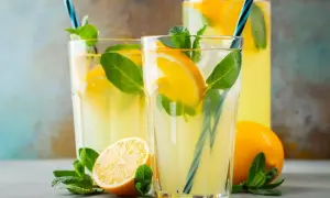 Dwa szklanki orzeźwiającej lemoniady z cytryną i miętą, obok cytryny i dzbanka z napojem.