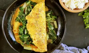 Omlet z serka wiejskiego z zielonymi warzywami na patelni.