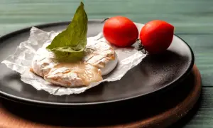 Grillowany ser camembert z pomidorkami koktajlowymi i bazylią na talerzu.