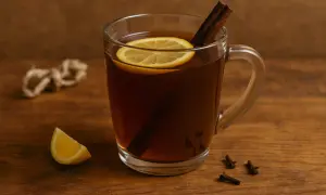 Szklanka gorącego napoju z cytryną i laską cynamonu na drewnianym tle.