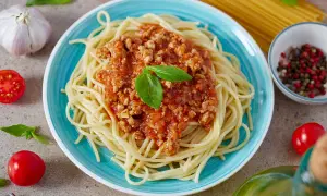 Spaghetti bolognese z mięsnym sosem pomidorowym, udekorowane bazylią, na niebieskim talerzu.