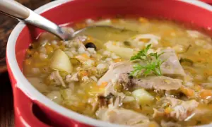 Miseczka domowego krupniku z mięsem, ziemniakami i kaszą jęczmienną, ozdobiona natką pietruszki.