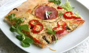 Kawałek pizzy z salami, papryką i serem na białym talerzu, ozdobiony sałatą.