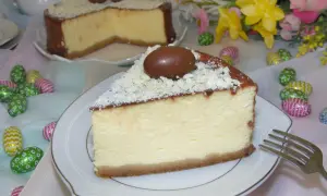Kawałek kremowego sernika z mascarpone, ozdobiony czekoladowymi jajeczkami i wiórkami białej czekolady, na talerzyku.