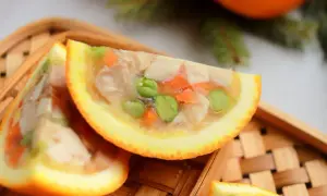 Kawałki galarety drobiowej z warzywami w skórkach pomarańczy na drewnianej tacce.