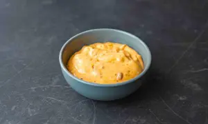 Pomarańczowy sos chipotle w niebieskiej miseczce na ciemnym tle.
