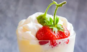 Deser zabaglione z truskawką i bitą śmietaną w szklance.