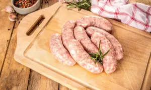 Surowa kiełbasa na desce, gotowa do parzenia. Obok gałązka rozmarynu, czosnek i przyprawy.